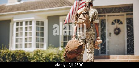 Vue arrière d'une maman militaire tenant un teddybear tout en se tenant à l'extérieur de sa maison avec ses bagages. Une femme courageuse est de retour à la maison après elle Banque D'Images