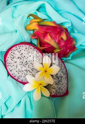 Un fruit de dragon en tranches et entier, décoré de fleurs de Frangipanni, sur fond turquoise Banque D'Images