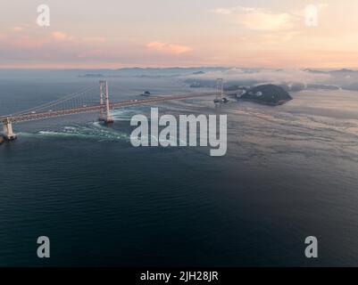 Un fort courant de marée circule sous le pont suspendu de Naruto au coucher du soleil Banque D'Images