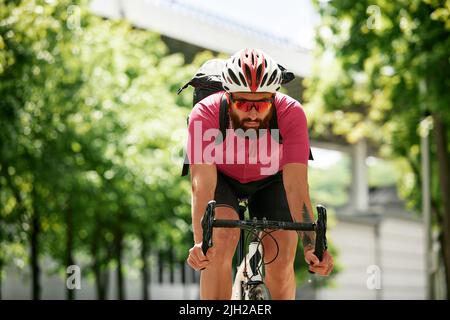 Homme dans des lunettes de soleil vitesse le long de la route sur un fond de parc d'été. Homme avec un vélo passe-temps manèges dans le parc. Banque D'Images