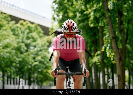 Homme dans des lunettes de soleil vitesse le long de la route sur un fond de parc d'été. Homme avec un vélo passe-temps manèges dans le parc. Banque D'Images