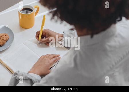 Une femme écrit ses pensées dans un journal au petit déjeuner . Banque D'Images