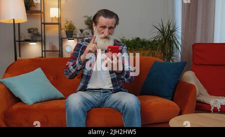 Grand-père senior homme portant des écouteurs faisant appel téléphone en ligne de conversation avec la famille assis à la maison salon canapé. Grand-père retraité âgé bénéficiant d'un haut-parleur mobile parlant Banque D'Images
