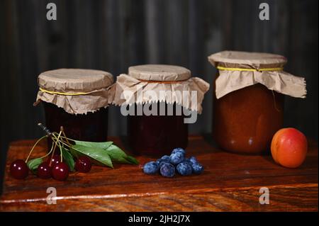 Collection de bocaux avec des confits faits maison avec des fruits de saison mûrs frais et des baies sur une surface en bois rustique. Banque D'Images