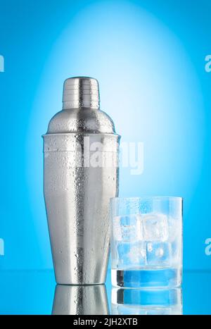 Shaker à cocktail et verre avec glaçons sur fond bleu Banque D'Images
