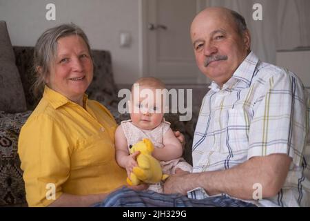 Couple senior avec petite-fille de bébé posant assis à la maison Banque D'Images