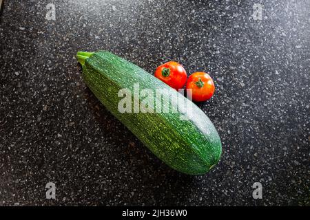 Courgettes rayées vertes et tomates rouges sur fond noir. Récolte estivale de légumes. Banque D'Images