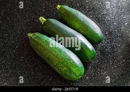 Courgettes rayées vertes sur une surface de table noire. Récolte estivale de légumes. Banque D'Images