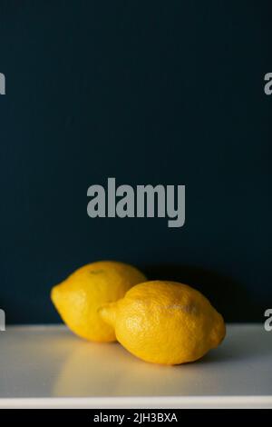 Durée de vie de deux citrons jaune vif sur une étagère blanche sur fond bleu foncé Banque D'Images