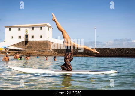 Une femme se dresse à l'envers sur une planche de surf à la plage de Porto da Barra à Salvador, Bahia. Banque D'Images