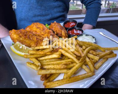 Vue rapprochée de poissons croustillants et de frites sur une table dans un restaurant en face d'un homme caucasien Banque D'Images