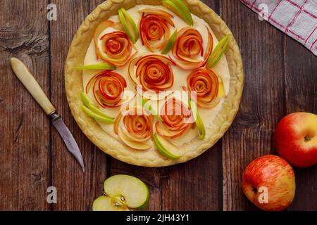 Sur une surface en bois, une tarte aux pommes cuite au four est décorée de pommes fraîches. Banque D'Images