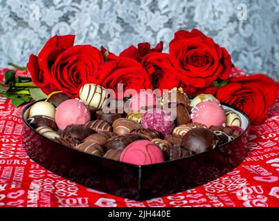 Boîte en forme de coeur de chocolats décalés et roses rouges sur fond de dentelle, la scène est définie pour le romantisme Banque D'Images