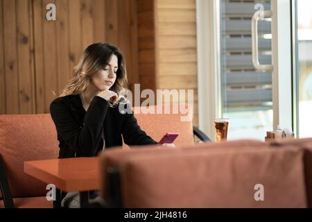 Une jeune fille dans un café utilise un smartphone pour les affaires, les achats en ligne, le transfert d'argent, les finances et les opérations bancaires en ligne. Profiter de votre temps libre dans un café Banque D'Images