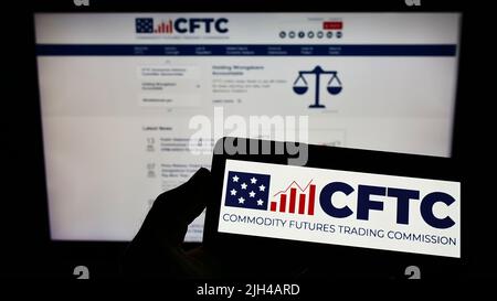Personne tenant un smartphone avec le logo de la US Commodity futures Trading Commission (CFTC) sur l'écran devant le site Web. Mise au point sur l'affichage du téléphone. Banque D'Images