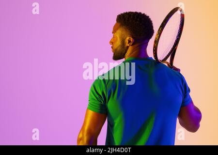 Image de la vue arrière d'un joueur de tennis afro-américain dans un éclairage au néon violet et jaune Banque D'Images