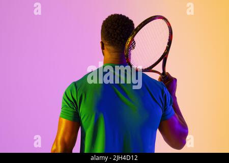 Image de la vue arrière d'un joueur de tennis afro-américain dans un éclairage au néon violet et jaune Banque D'Images