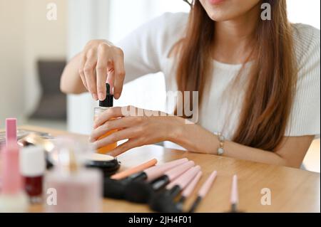 Une femme asiatique professionnelle maquilleuse ou blogueur de beauté tenant une bouteille de sérum cosmétique, faisant son tutoriel de maquillage à la maison. Image rognée Banque D'Images