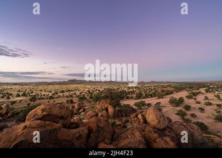 Un magnifique coucher de soleil aux couleurs violettes dans le ciel et aux rochers au premier plan. Vue sur le désert environnant en Namibie, pendant la saison des pluies. L Banque D'Images