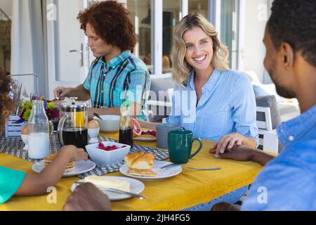 Bonne jeune femme multiraciale touchant la main de l'homme tout en prenant le petit déjeuner en famille à la table à manger Banque D'Images