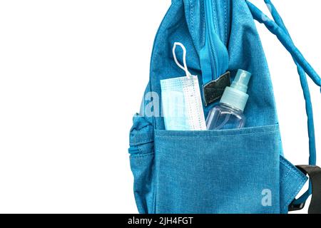 Poche latérale de sac à dos bleu pour étudiants avec masque facial et petite bouteille d'alcool, sac à dos avec vue latérale, image isolée sur fond blanc. Co Banque D'Images