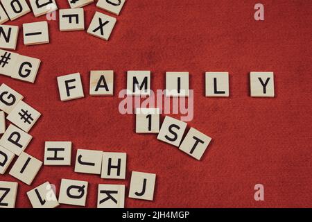 Phrase 'Family 1st' composée de carreaux de bois avec des lettres sur fond de feutre rouge Banque D'Images