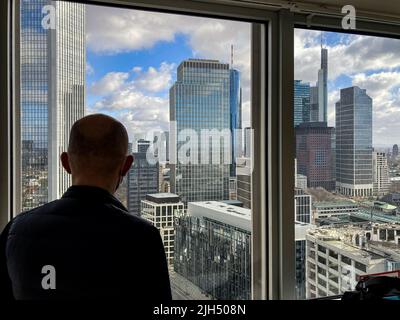 21 février 2022, Hessen, Francfort-sur-le-main : un homme regarde par la fenêtre d'une tour de bureau à une partie de la ligne d'horizon de Francfort. Photo: Frank Rumpenhorst/dpa Banque D'Images