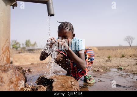 Une petite fille africaine éclabousse avec de grandes quantités d'eau propre dans un puits d'eau douce situé dans une région aride sub-saharienne Banque D'Images