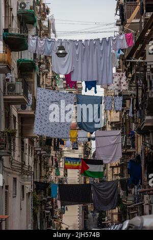 Blanchisserie et drapeaux suspendus sur des cordes à linge au-dessus de la rue étroite dans le centre historique de Naples, Italie. Banque D'Images