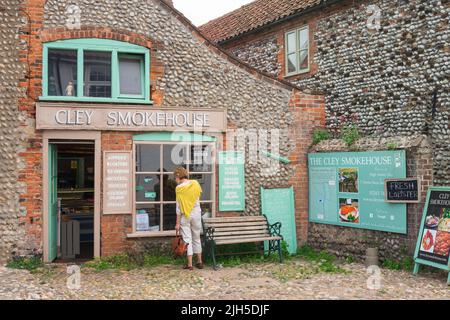 CLEY Smokehouse, vue d'une femme à CLEY à côté de la mer regardant dans la fenêtre de la populaire CLEY Smokehouse, côte nord de norfolk, Angleterre Royaume-Uni Banque D'Images