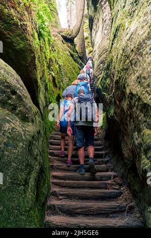 Adersbach, République Tchèque, 4 juillet 2022: Un groupe de touristes monte un escalier raide entre d'énormes blocs de grès dans la ville rocheuse d'Adersbach Banque D'Images