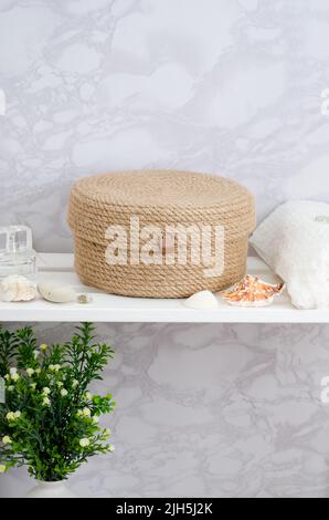 Panier en jute tricoté à la main pour accessoires et cosmétiques dans la salle de bains sur un rack en bois blanc. Banque D'Images