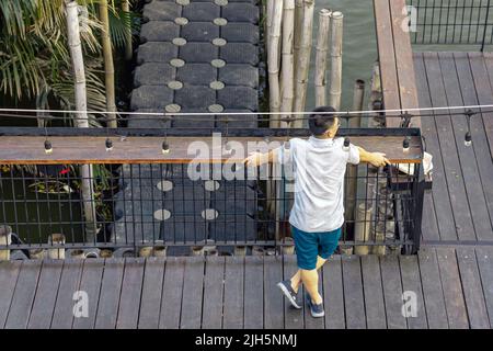Vue arrière de l'homme asiatique se détendant et se détendant au bord de la rivière. Détendez-vous en vacances d'été pour un homme adulte en profitant de la liberté. Des gens heureux à l'extérieur r Banque D'Images