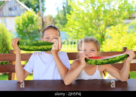 Les enfants mangent de la pastèque en été. Des enfants satisfaits avec un grand morceau de pastèque sur le fond du jardin Banque D'Images