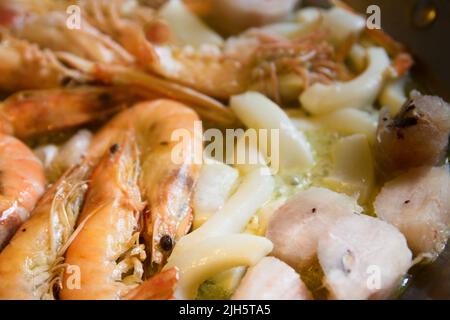 Détail de quelques coquillages (crevettes, poisson, seiche) qui commencent à cuire dans une paella de fruits de mer Banque D'Images