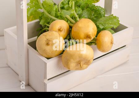 Navet jaune frais avec tiges et feuilles vertes dans une boîte sur fond blanc en bois. Banque D'Images