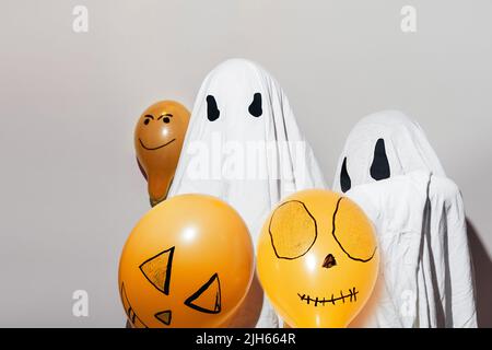 Joyeux Halloween, automne. Enfants vêtus de costumes blancs fantômes et de ballons orange peints. Différentes émotions de joie, de colère, de rire. Costumes faits à la main.décoration festive, concept de fête. Banque D'Images