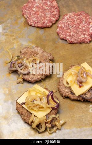 Hamburger frit avec fromage et oignons frits et deux hamburgers crus sur fond rouillé. Vue de dessus. Banque D'Images