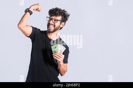 Homme excité avec de l'argent dans sa main isolé. Un homme heureux avec de l'argent levant son poing, souriant homme beau avec de l'argent en main, étonnait les gens avec Banque D'Images