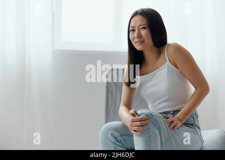 Crampes orteil cassé os cassé dans la jambe. Souffrance tourmentée bronzée belle jeune femme asiatique touche la jambe à la maison intérieur salon. Blessures faibles Banque D'Images