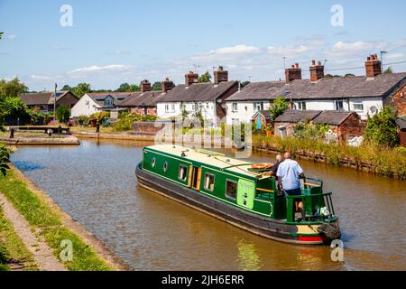 Les gens sur un canal narrowboat vacances en passant par des chalets du côté du canal à l'approche de l'écluse 63 à Malkins Bank Cheshire sur le canal Trent et Mersey Banque D'Images