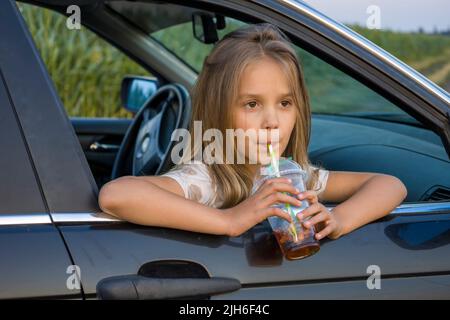 Une fille avec un verre en plastique d'un cocktail dans une voiture Banque D'Images