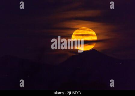 Grande lune de récolte s'élevant au-dessus des montagnes de l'Arizona, partiellement couverte de nuages Banque D'Images