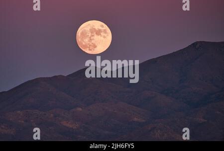 Grande lune de Hunter qui s'élève au-dessus des montagnes de l'Arizona, partiellement couverte de nuages Banque D'Images