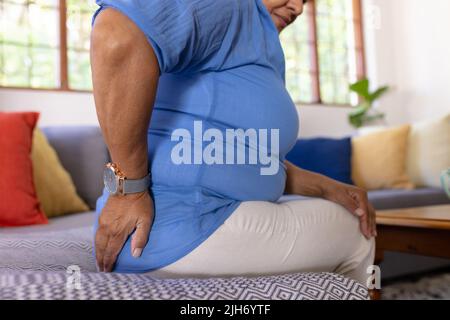 Section médiane de la femme biraciale mature avec le bas du dos touchant le dos tout en étant assis sur le canapé à la maison Banque D'Images