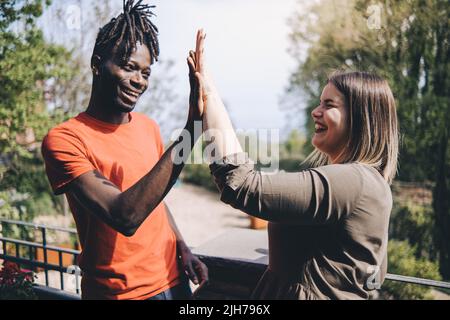 Profil vue latérale de l'homme africain heureux faisant geste de salutation donner haut cinq avec sourire et jeune femme caucasienne. Deux meilleurs amis qui se claque les mains, Banque D'Images