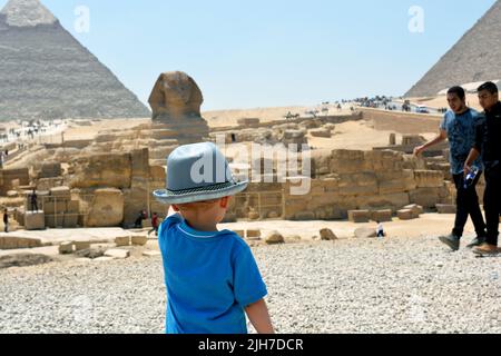 Giza, Egypte, juin 27 2017 : enfant touristique dans le plateau de Giza sur la rive ouest du Nil face à un Sphinx flou et aux pyramides de l'ancien W Banque D'Images