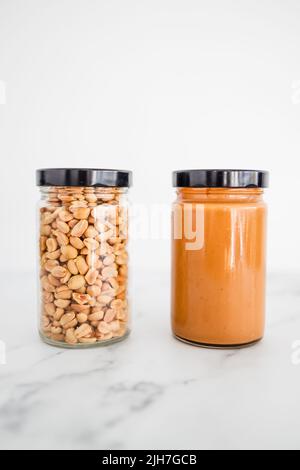 bocaux en verre avec arachides et beurre d'arachide sur fond de marbre blanc, ingrédients de base naturels sains de garde-manger Banque D'Images