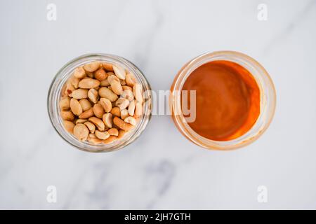 bocaux en verre avec arachides et beurre d'arachide sur fond de marbre blanc, ingrédients de base naturels sains de garde-manger Banque D'Images