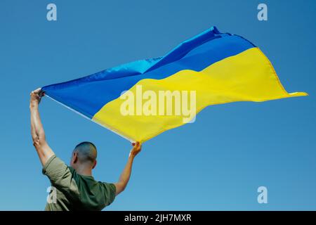 gros plan d'un homme, vu de l'arrière, agitant le drapeau ukrainien sur le ciel au-dessus de sa tête, en un jour ensoleillé Banque D'Images
